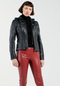 Schwarze Lederjacke mit Kapuze, ausgestattet mit zwei Reißverschlusstaschen und einem taillierten Design. Kombiniert mit glänzenden roten Lederhosen. Glatte Textur.