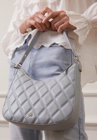 Harmaa nahkakäsilaukku, jossa on tikattu kuosi, kaareva muoto ja olkahihna. Varustettu kultaisilla varusteilla.