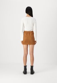 Jupe mini en suede marron avec une waistband élastique, associée à un haut à manches longues blanc côtelé et des bottines noires.