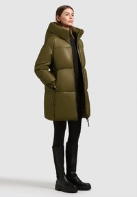 Olijfgroene donsjas met een hoge kraag en een aansluitend model. Voorzien van ritssluiting, zijzakken en een licht getailleerde taille.