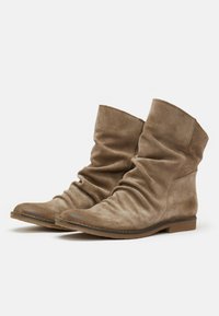 Bottines en daim marron avec un design loose, un bout pointu et une semelle plate. Remarquables pour leur texture douce et leur style minimaliste.