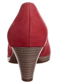 Scarpa con tacco alto in suede rosso dal design affusolato, con un tacco impilato texturizzato e dettagli di cucitura visibili lungo la parte posteriore.