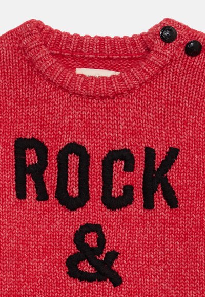 Pull rouge en maille avec texte noir "ROCK &" et deux boutons noirs près de l'encolure ronde sur l'épaule droite.
