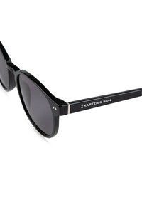 Černé sluneční brýle s kulatými čočkami, s lesklým povrchem, kovovým akcentem na spáncích a s názvem značky "KAPTEN & SON" zobrazeným.