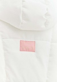 Biała, pikowana kurtka puchowa z prążkowaną fakturą i różową naszywką z napisem. Projekt z kapturem i pikowanymi panelami.