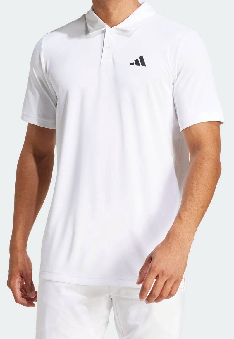 Homme portant un polo blanc uni à manches courtes avec un petit logo Adidas noir sur la poitrine gauche.