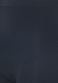Texture de tissu bleu marine foncé en gros plan avec des reflets subtils de lumière et des détails de couture fines.