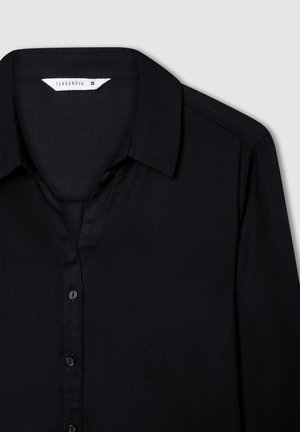 Camicia nera con bottoni, dotata di colletto, realizzata in tessuto morbido, con una pattina frontale con bottoni neri e un'etichetta di misura all'interno del colletto.