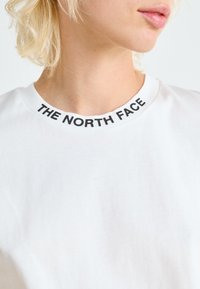 Witte katoenen t-shirt met een zwarte ribbelkraag waarop "THE NORTH FACE" is gedrukt. Close-up toont de textuur en pasvorm rond de nek.