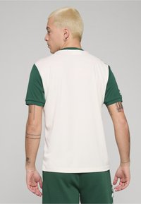 Biały sportowy T-shirt z zielonymi krótkimi rękawami, z okrągłym dekoltem i gładką tkaniną. Widok z tyłu pokazuje prosty design bez widocznych logo.