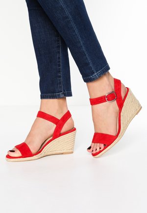 Sandales compensées en daim rouge avec brides à la cheville, semelle en jute tressé, bout ouvert et légère plateforme. Positionnées sur un fond blanc.
