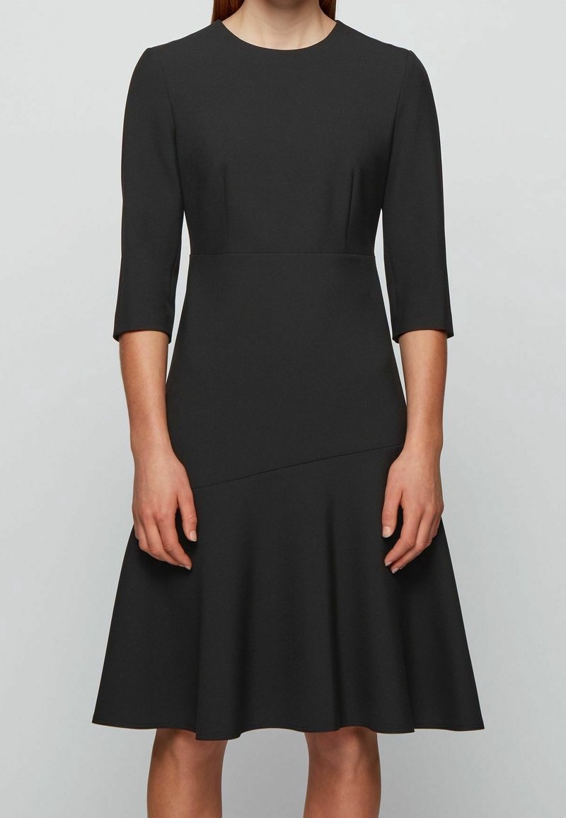 Svart klänning med trekvartsärmar, figursydd liv och utsvängd kjol. Tillverkad av mjukt tyg med rund halsringning och sömdetaljer.