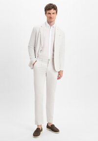 Light-colored linen suit with a tailored fit, paired with a white button-up shirt and brown suede loafers. Smooth texture, minimalist style.