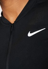 Black athletic bodysuit with a zip front, featuring a small white Nike logo on the chest. Smooth, stretchy fabric with a fitted design.