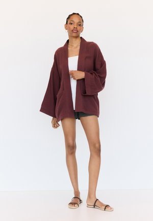 Bordeaux kimono-stijl jas in lichtgewicht textuurstof. Kenmerken zijn brede mouwen, een open voorkant en twee voorkeurszakken.