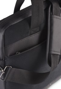 Der Innenraum der schwarzen Laptoptasche zeigt das gepolsterte Fach, eine Reißverschlusstasche und den verstellbaren Schultergurt mit Metallverschluss.