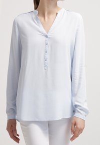Camicia azzurro chiaro a maniche lunghe con scollatura a V, chiusura a bottoni e maniche con polsini. Tessuto morbido e liscio con una vestibilità comoda.