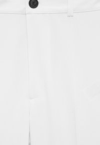 Białe spodnie o gładkiej fakturze, z czarnym zapięciem na guzik i prostym krojem, odsłaniające część pasa i obszaru kieszeni.