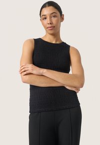 Černý top bez rukávů s texturovanou látkou, s kulatým výstřihem a nařasenými detaily. V kombinaci s černými kalhotami má tento outfit elegantní vzhled.