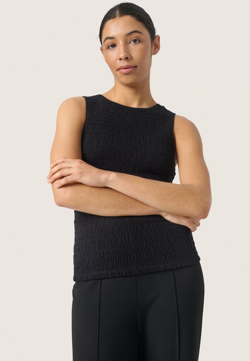 Svart ärmlös topp med texturerad tyg, med rund halsringning och rynkade detaljer. Tillsammans med svarta byxor har outfiten en elegant design.