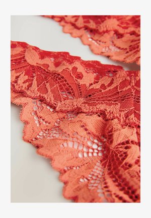 Material din dantelă roșie cu modele florale și margini ondulate, evidențiind texturi complicate și o țesătură deschisă și delicată.
