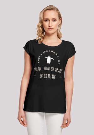 Schwarzes T-Shirt mit aufgerollten Ärmeln, mit einem weißen Pinguin-Graphic und dem Text: "Knut & Jan | Hamburg | GO SOUTH POLE 2023" in hellen Farben.