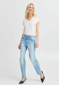 Blusa bianca a V con maniche corte, abbinata a jeans a gamba dritta azzurri chiari e décolleté neri a punta. Outfit semplice e casual.