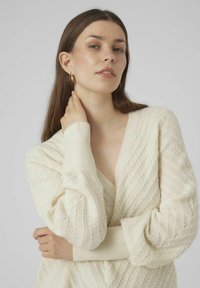 Cream, knitted sweater with a V-neck, featuring ribbed cuffs and a textured pattern. Long sleeves and relaxed fit.