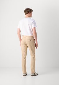 Beige chinos med rett passform, laget av bomull. Har baklommer med knappdetaljer, kombinert med en enkel hvit t-skjorte og casual sko.