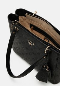 Musta keinonahkainen käsilaukku, jossa on kohokuvioidut kuviot, kultaiset metalliosat, kaksinkertaiset kahvat ja beige sisusta, jossa on useita taskuja.