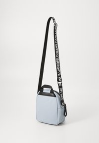 Svetlomodrá syntetická crossbody taška s čiernymi akcentmi, hornou rúčkou a čiernym popruhom s bielym brandovaním. Kompaktný tvar a uzávery na zips.