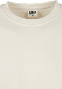 Gros plan sur un sweat-shirt col rond uni blanc cassé, avec une étiquette "Urban Classics Organic" visible, taille M.