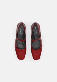 Rode gepatineerde leren schoenen met een ronde neus, vierkante vorm en verstelbare band. Zwarte gevoerde binnenkant en merkinleg.
