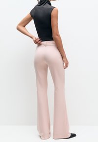 Haut noir sans manches et pantalon évasé rose pâle. Le pantalon présente une taille ajustée et une texture lisse, assorti à des chaussures noires à bouts pointus.
