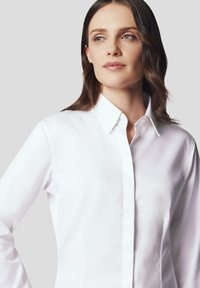Biała koszula z guzikami, o sztywnym kołnierzu, długich rękawach i gładkim materiale, z dopasowanym krojem i minimalnymi detalami.