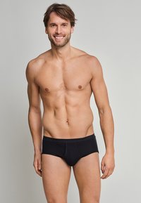 Schwarze Slips aus weichem Stoff mit einer engen Passform, ausgestattet mit einem breiten, elastischen Bund, der mit dem Markennamen geprägt ist, sowie einer Nahtdetails vorne.
