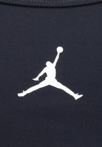 Čierna športová tkanina so výrazným bielym logom Jumpman. Dizajn obsahuje hladký, štýlový siluet s basketbalom.