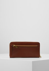 Portefeuille en cuir marron avec une texture lisse, doté d'une fermeture éclair dorée et d'accents cousus, de forme rectangulaire plate avec une poche latérale.
