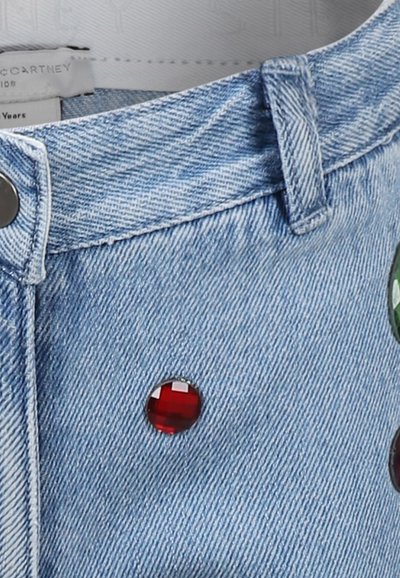 Shorts in denim con un lavaggio blu chiaro, caratterizzati da accessori neri e gemme decorative rosse e verdi sulla parte anteriore.