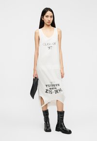 Rochie albă fără mâneci, tip top, cu imprimeu "CLASA '97". Design cu tiv despărțit, material fluid, asortată cu cizme negre până la genunchi.