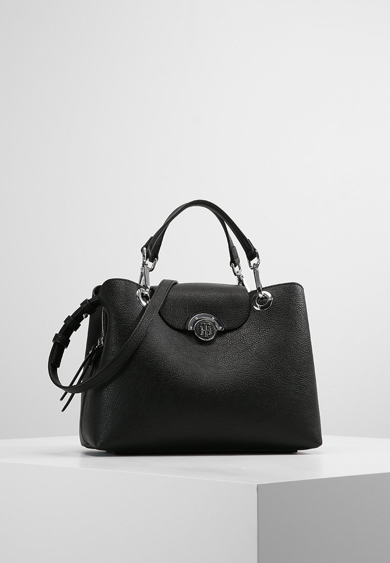 Bolso de cuero negro con acabado texturizado, doble asa superior, correa de hombro ajustable y un adorno de logo en tono plateado en el frente.