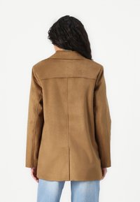 Brown faux suede jacket with a tailored design, single back vent, and notched lapels. Features long sleeves and a straight silhouette.