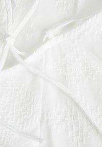 Tela de algodón blanca con un patrón texturizado; cuenta con lazos para abrochar; superficie suave con sutiles detalles dimensionales.