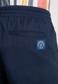 Námořnické modré šortky s elastickým pasem, se zadní kapsou a obdélníkovou nášivkou s nápisem "Tommy Jeans USA." Hladký povrch.