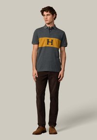 Šedé polo tričko so žltým stredovým pruhom a námorníckym golierom; zdobí ho veľké logo "H" na hrudi. Nosené s tmavohnedými nohavicami a hnedými topánkami.