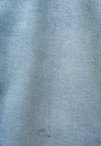 Tela de mezclilla azul claro que muestra un sutil patrón de tejido diagonal con un ligero desvanecimiento y dos pequeños acentos cosidos en la parte inferior.