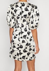 Robe courte en satin blanc avec imprimé floral noir, manches ballon et coupe ajustée avec une fermeture discrète au dos.