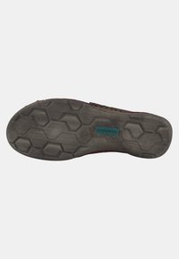 Semelle de chaussure en caoutchouc, présentant un motif hexagonal et une surface texturée. Gris foncé avec une étiquette de logo en teal intégrée.