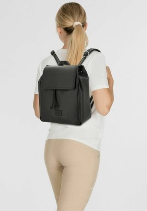 Sac à dos en cuir noir texturé avec des bretelles réglables, fermeture à rabat et détail de cordon. Shape rectangulaire compact, minimalisme en matière de marque.