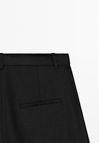 Pantaloni neri su misura con vita dotata di passanti per cintura e una tasca posteriore a filetto, fotografati su sfondo bianco semplice.